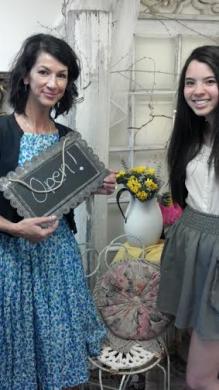 Two women smiling at camera, one holds an Open sign