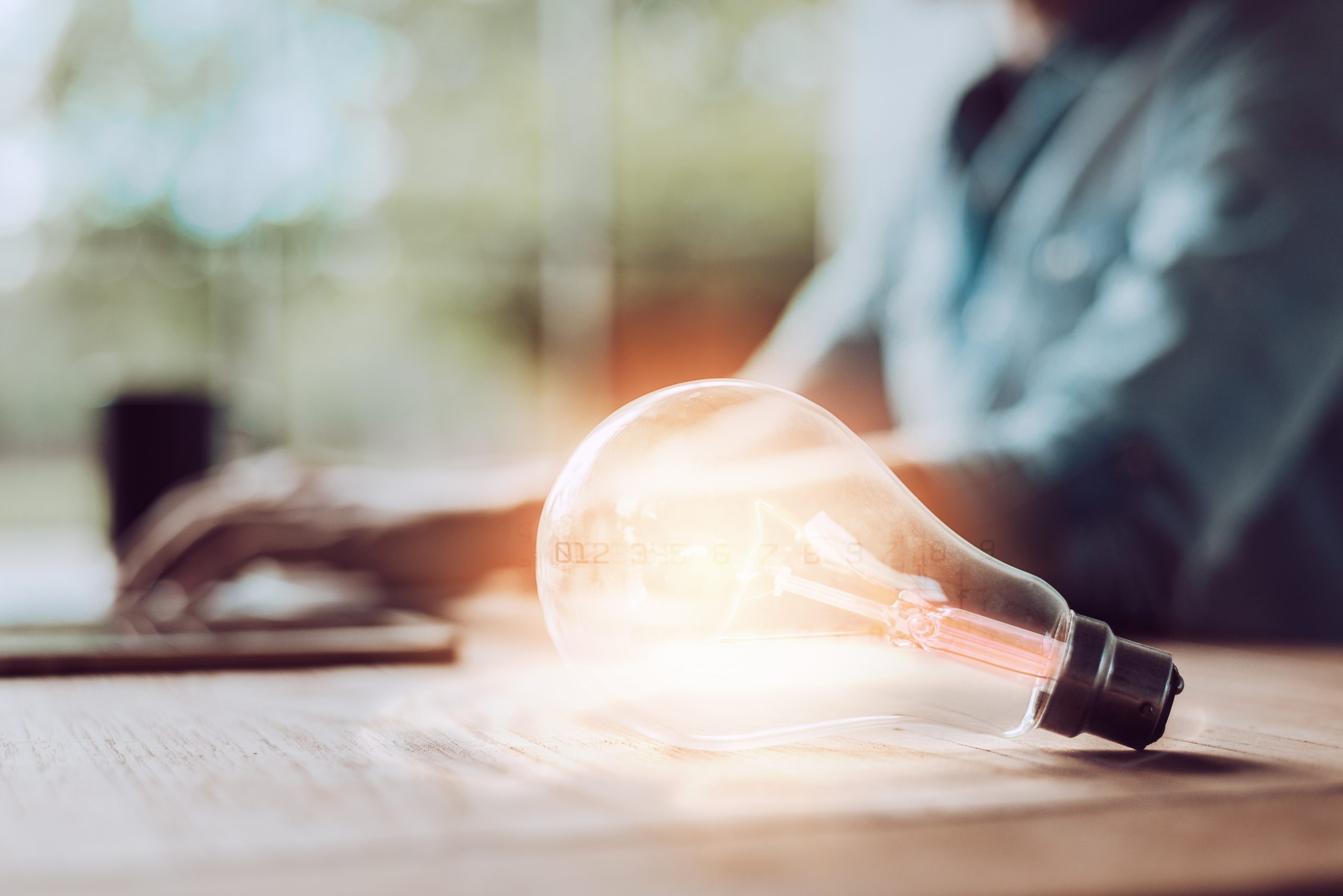 lightbulb on table in front on man on computer